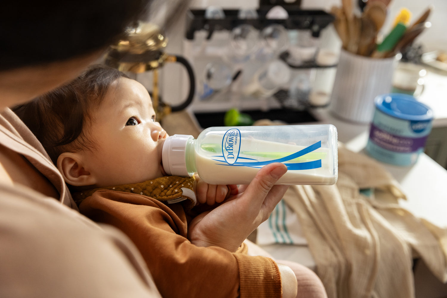Mom feeding baby in kitchen with Dr. Brown's bottle